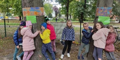Powiększ grafikę: Zdjęcie przedstawia grupę dzieci stojące przy dwóch drzewach, które brały udział w akcji